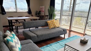 Una sala de estar moderna con un sofá gris, una mesa de centro de madera y vistas de la ciudad a través de grandes ventanales.