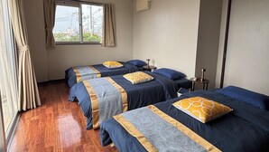 Habitación de hotel con tres camas, una ventana con cortinas, suelo de madera e iluminación empotrada en el techo.