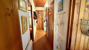 A narrow hallway with wooden doors and walls, decorated with framed pictures and macramé wall hangings. - Bright T2 Apartment - 200m from Beach, 4 pax (Argelès-sur-Mer)
