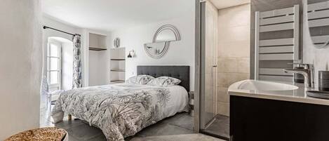 A modern bedroom with a large bed, a bedside table, a mirror, and a bathroom with a sink and mirror.