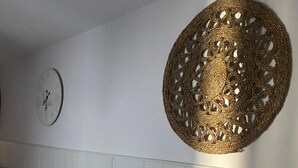 En spiseplads med et bord dækket af et blomstret duge, to hvide stole, et vægur og et stort vægtæppe.