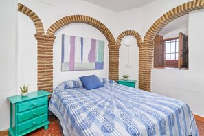 Een slaapkamer met een bed, een nachtkastje, een wandklok en een raam met open deur.