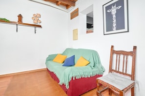 Een kamer met een rode bank, een houten stoel, een foto van een giraffe in een lijst, een plank met decoratieve objecten, en een bord op de muur.