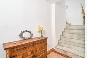 Een houten dressoir met lades, een spiegel en een vaas met bloemen voor een witte muur.
