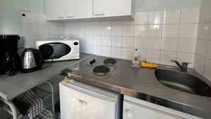 Et kompakt køkken med hvide skabe, en mikrobølgeovn, kaffemaskine, gasblus og vask.