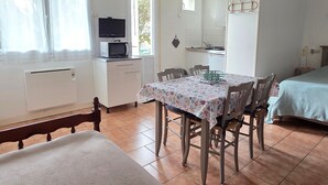 Ein kleines Zimmer mit Esstisch, Stühlen, einem Bett, einem Fernseher, einer Mikrowelle und einer kleinen Küchenzeile.