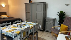 Ein kleiner, gut beleuchteter Raum mit einem Bett, einem Tisch mit Stühlen, einem Schrank und einer Topfpflanze.