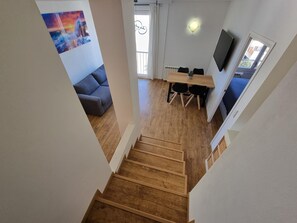 A staircase leading to a living area with a sofa, a dining table with chairs, a TV, and a window with curtains. - Charming apartment in L'Escala, near the port and beach (L'Escala)