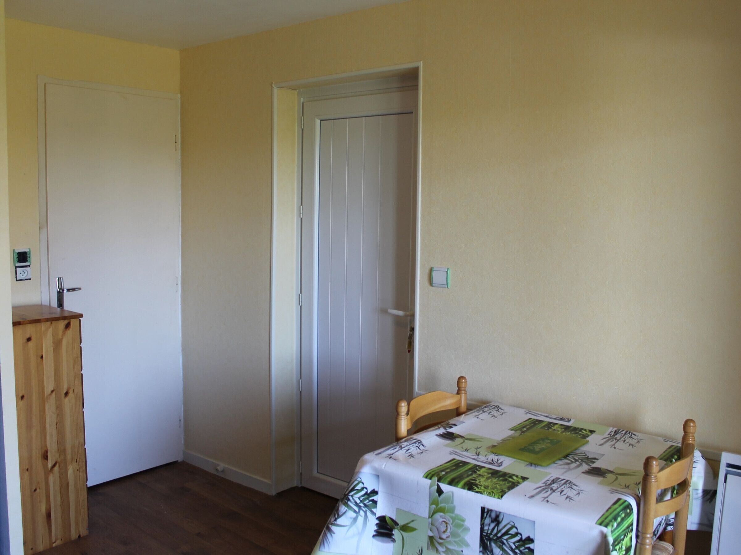A small room with a wooden cabinet, a door, and a table with a floral tablecloth.