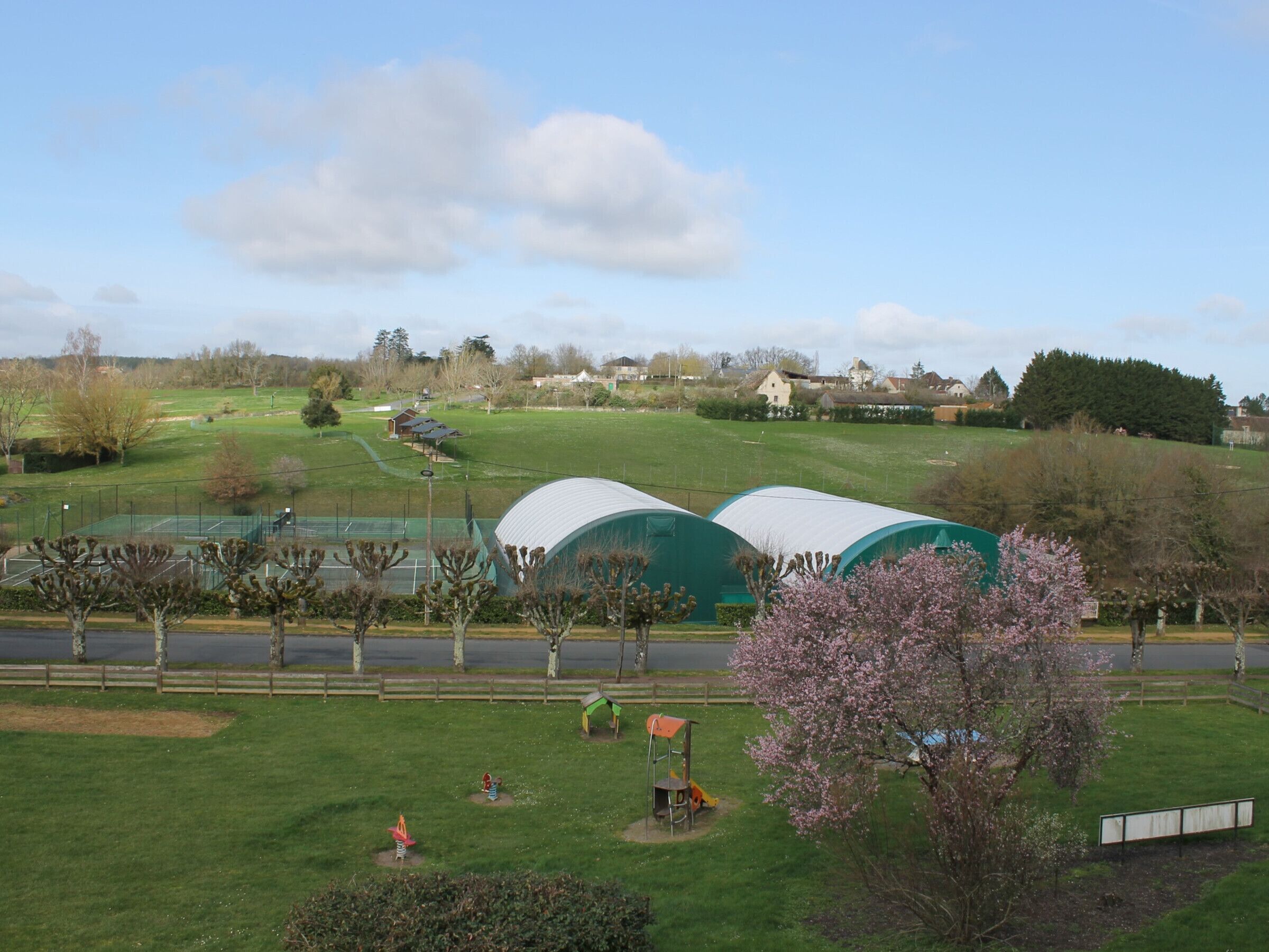 A park with green fields, a playground, and a tennis court.