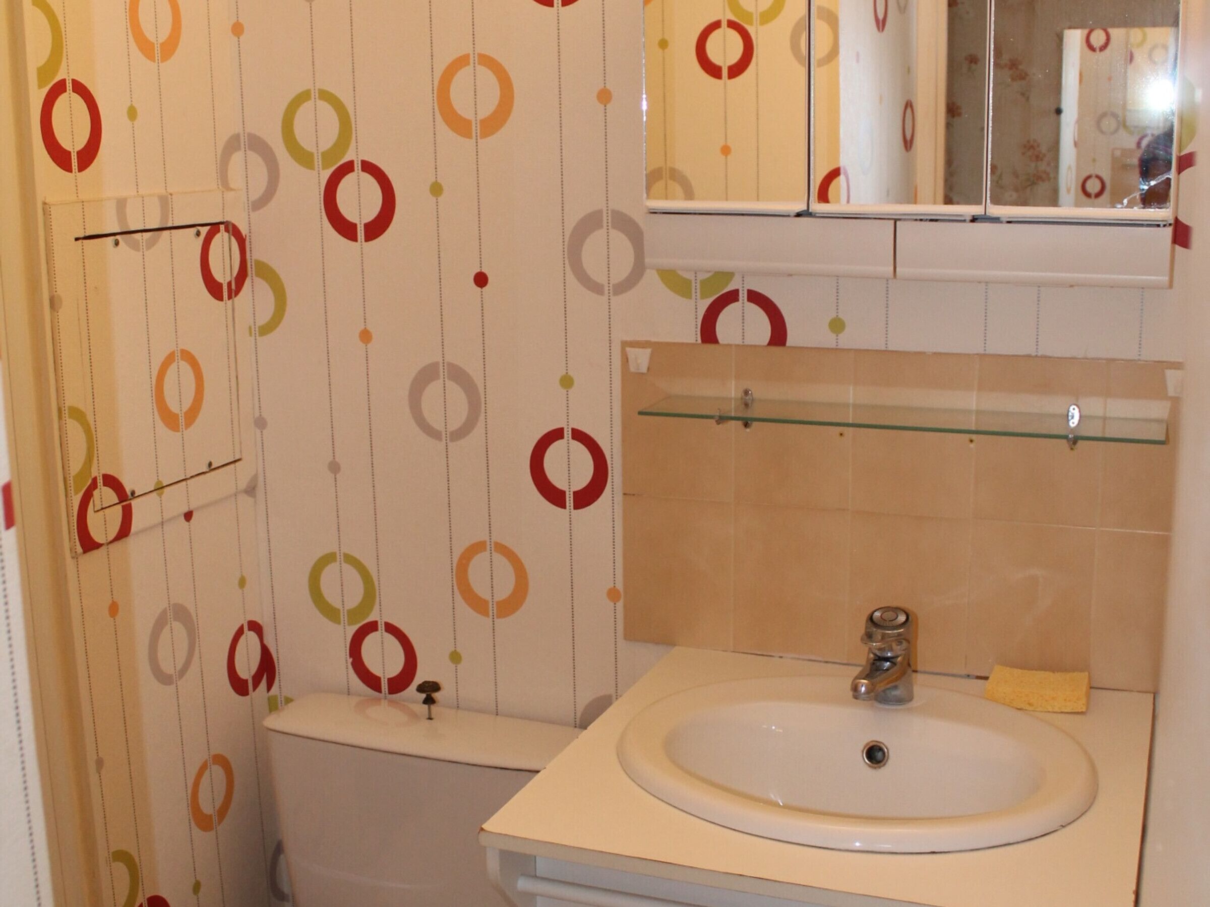 A bathroom with a white sink, mirror, and toilet. The walls have a circular pattern.