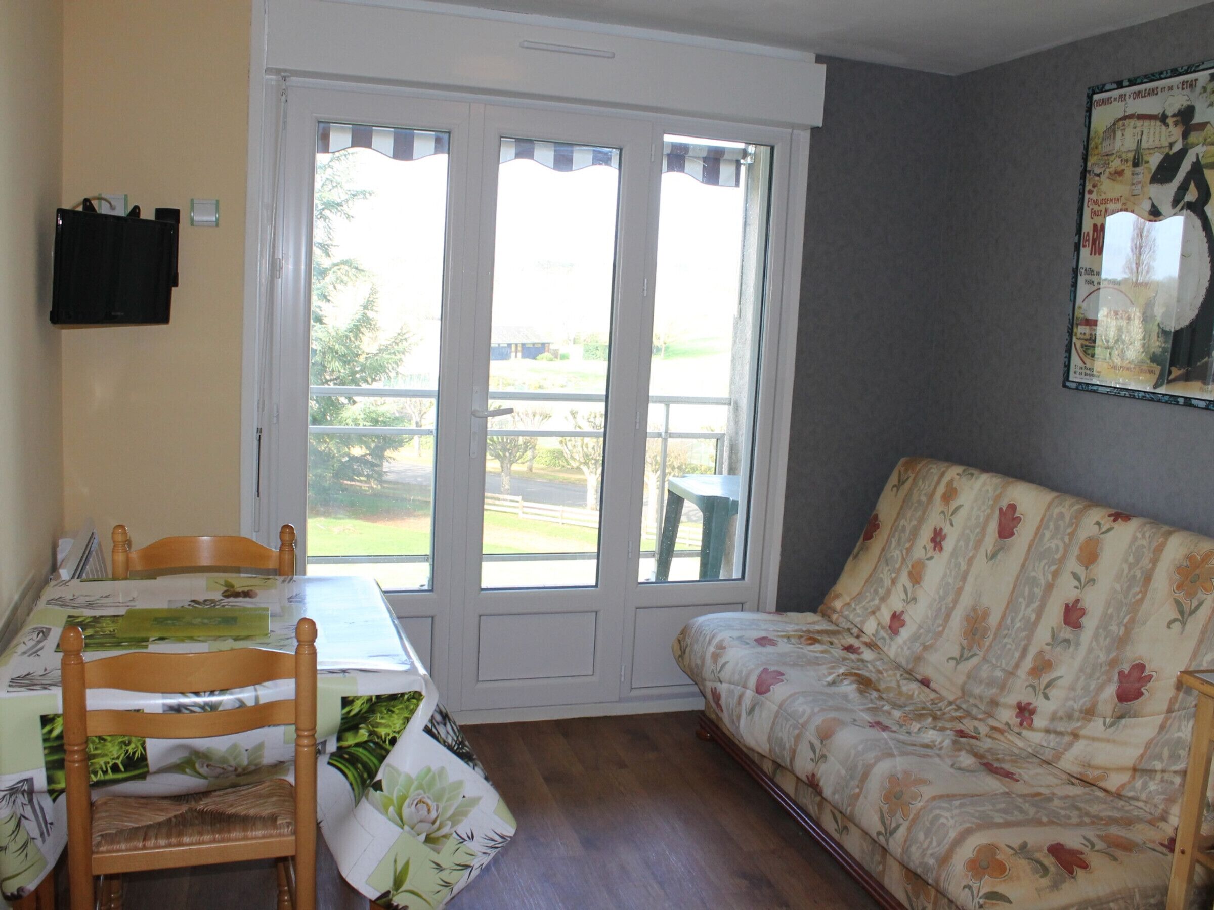 A room with a dining table, a floral sofa, and a large window with a view of the outdoors.