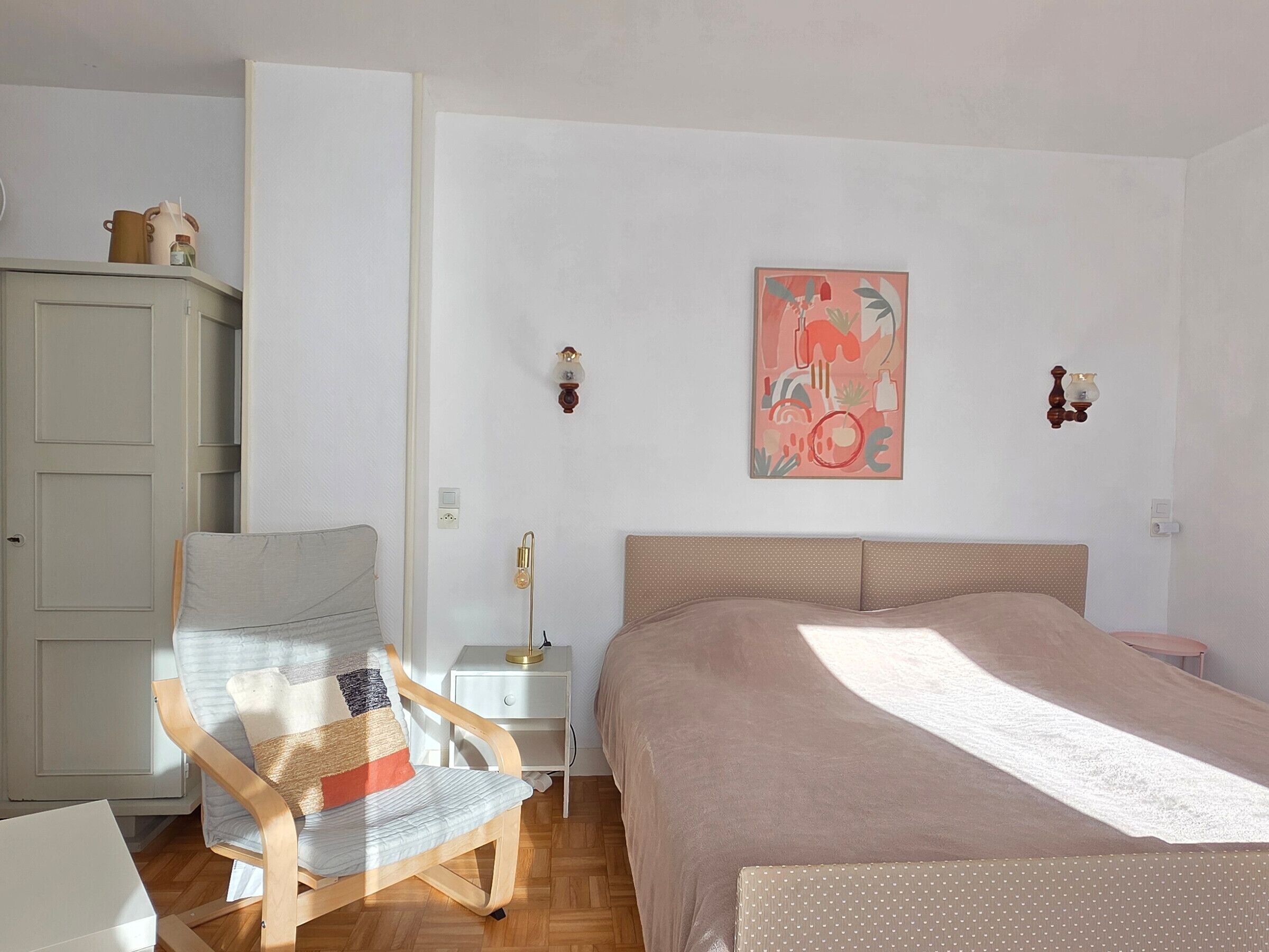 Une chambre à coucher comprenant un lit, une chaise, une table de chevet, une armoire et une œuvre d’art murale.