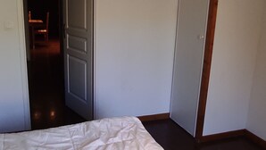 A bedroom with a bed, a door leading to a hallway, and a chair in the background. - Calm apartment in Super Besse, 5 people, parking and pool (Besse-et-Saint-Anastaise-Super Besse)