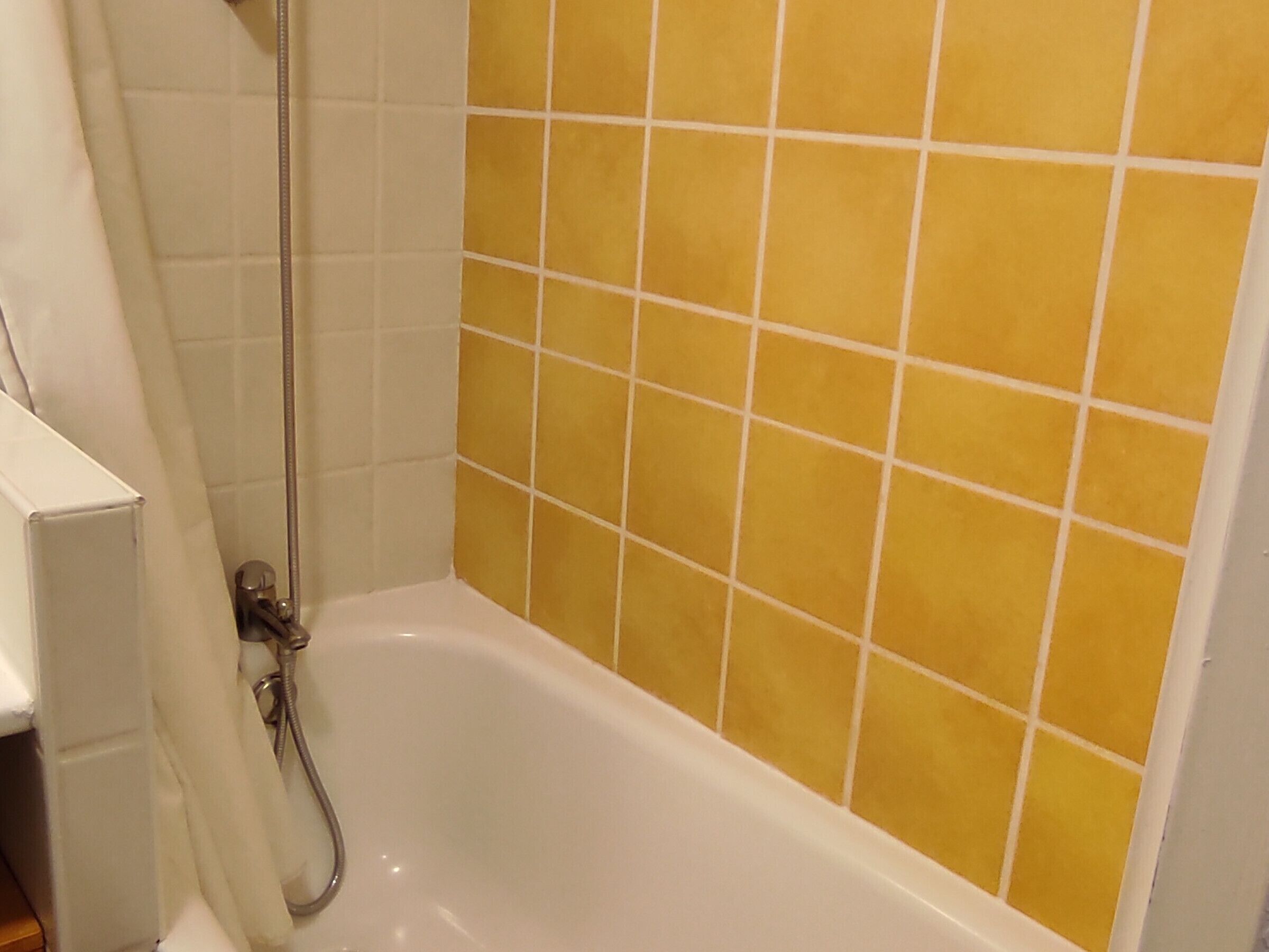 A bathroom with a white bathtub, yellow tiled walls, and a shower area.
