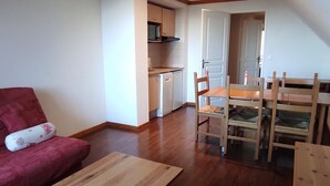 A compact living space with a dining area, kitchenette, and a red sofa. - Calm apartment in Super Besse, 5 people, parking and pool (Besse-et-Saint-Anastaise-Super Besse)
