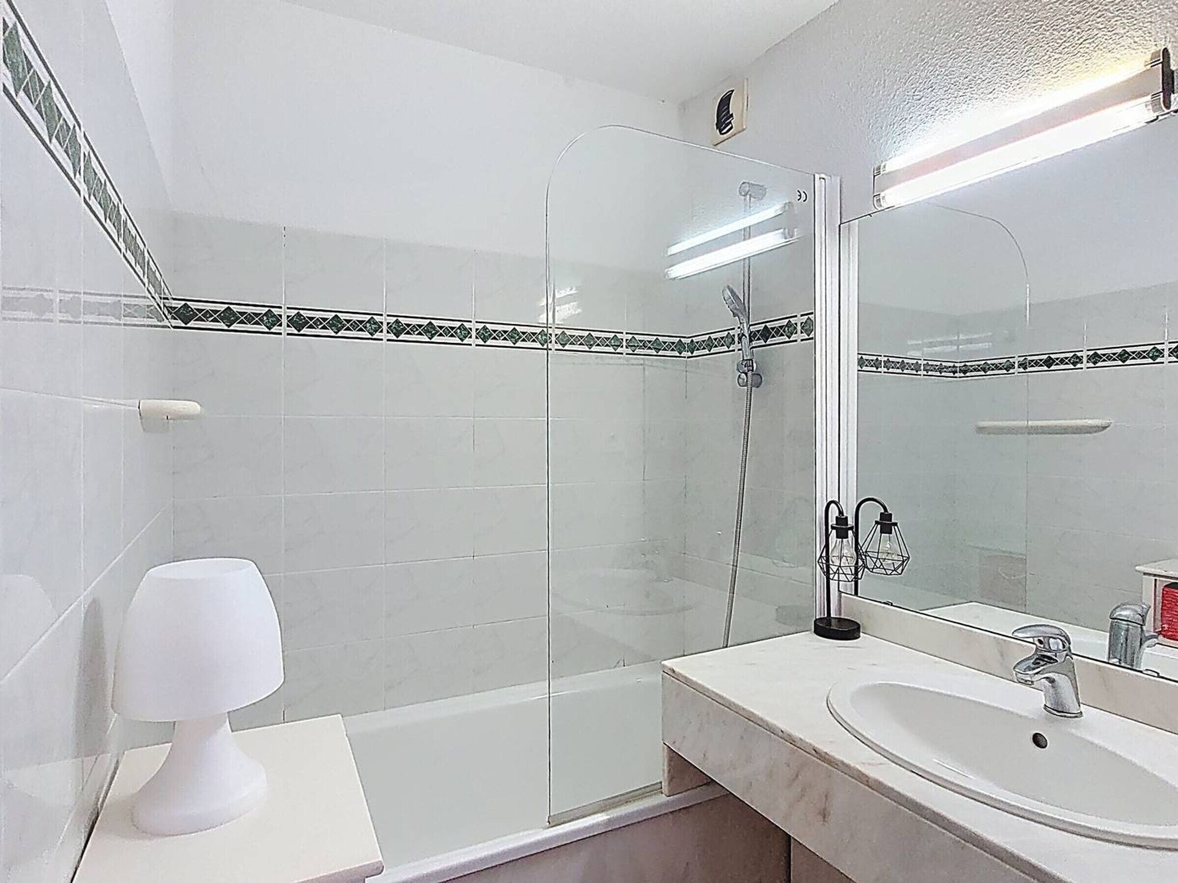 Un baño con lavamanos blanco, un espejo y cabina de ducha.