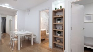 A modern, minimalist room with a white dining table, chairs, and a built-in wooden shelf with decorative items. - Amazing apartment in the centre of Seville (centro)