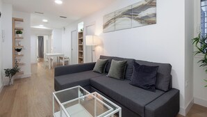 A modern living room with a grey sofa, a glass coffee table, and a dining area in the background. - Amazing apartment in the centre of Seville (centro)