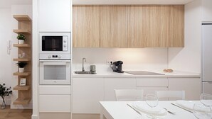 A modern kitchen with white cabinetry, a built-in microwave, oven, and a coffee machine. There is a dining table set with plates, glasses, and cutlery. - Amazing apartment in the centre of Seville (centro)