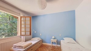 A room with a bed, a window with a view of trees, a bedside table with a lamp, and a wall with a blue accent. - Villa for 6 guests in Moliets with pets allowed (Moliets-et-Maa)