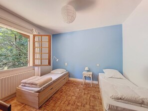 A room with a bed, a window with a view of trees, a bedside table with a lamp, and a wall with a blue accent.