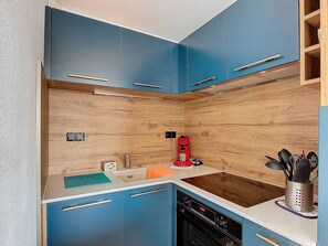Eine kleine Küche mit blauen Schränken, einer Holz-Spritzschutzwand, einer Kaffeemaschine und einem Spülbecken.