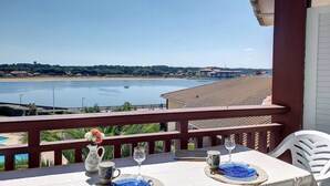 Varanda com mesa posta para dois, com vista para uma praia e um corpo de água.