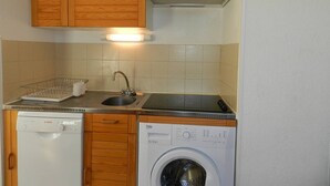Een compacte keuken met houten kastjes, een Bosch vaatwasser, een Beko wasmachine en een spoelbak met afwasservice.