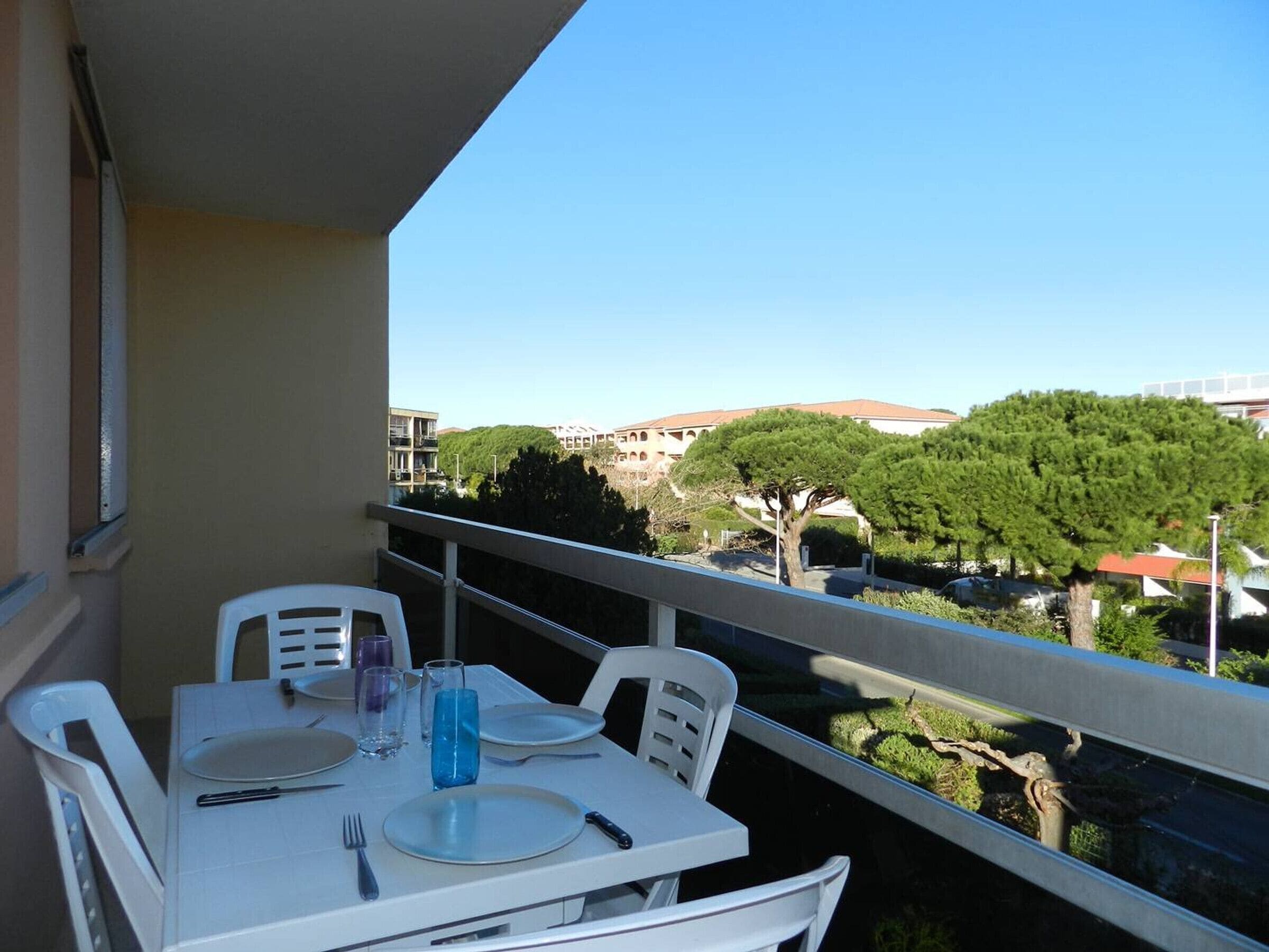 Un balcón con una mesa preparada para dos personas, con vistas a un paisaje urbano con edificios y árboles.