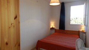 Een slaapkamer met een bed, een raam met gordijnen, een hanglamp en een nachtkastje met een lamp.
