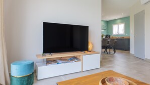 A modern living room with a flat-screen TV, a wooden coffee table, and a kitchen in the background. - Villa "Gîte Des Clapas – Lisa" with Wi-Fi and Air Conditioning (Balazuc)
