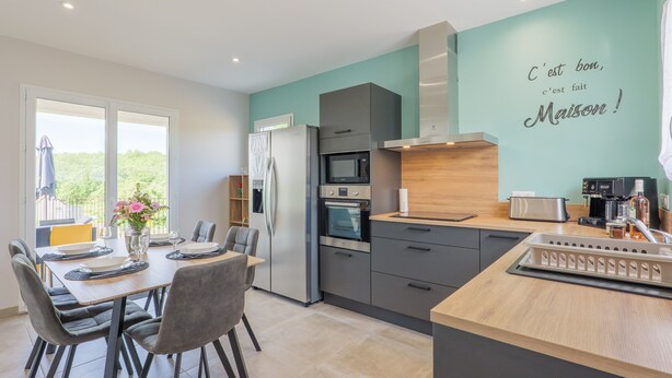 A modern kitchen with a dining area, a large window, and a teal accent wall. - Villa "Gîte Des Clapas – Lisa" with Wi-Fi and Air Conditioning (Balazuc)