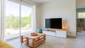 A modern living room with a television, a wooden coffee table, and a sliding glass door leading to an outdoor area. - Villa "Gîte Des Clapas – Lisa" with Wi-Fi and Air Conditioning (Balazuc)