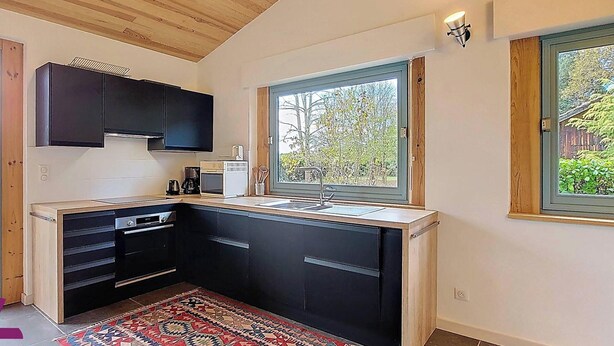 Uma cozinha moderna com armários pretos, forno embutido e uma grande janela com vista para o verde lá fora.