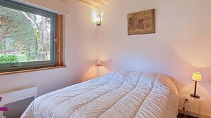Quarto com uma janela grande, uma cama, luminária na parede e um quadro.