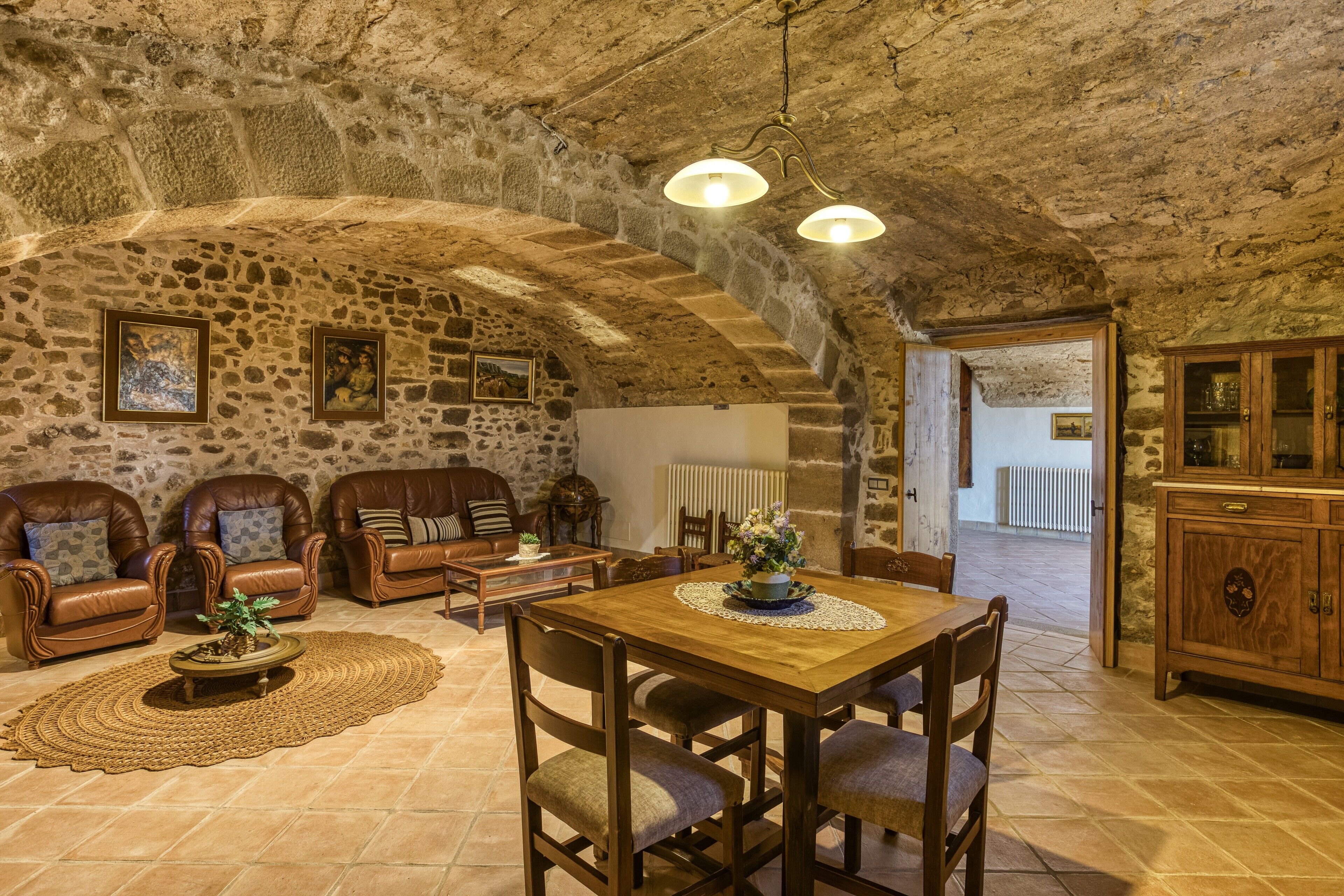 A rustic stone interior with leather sofas, a wooden dining table, and a stone fireplace.