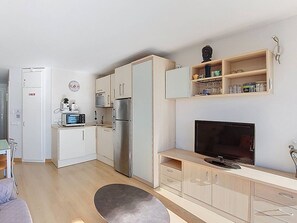Eine kleine Küche mit Mikrowelle, Kühlschrank und Spüle. Ein Fernseher steht auf einem Holzboden und ein Regal mit Gläsern ist ebenfalls vorhanden.