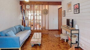 Ein Wohnzimmer mit einem blauen Sofa, einem Couchtisch, einem Fernseher auf einem Schrank und Holzdielen.