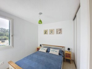 Ein Schlafzimmer mit einem Einzelbett, einem Fenster, einer grünen Pendelleuchte und drei gerahmten Bildern an der Wand.