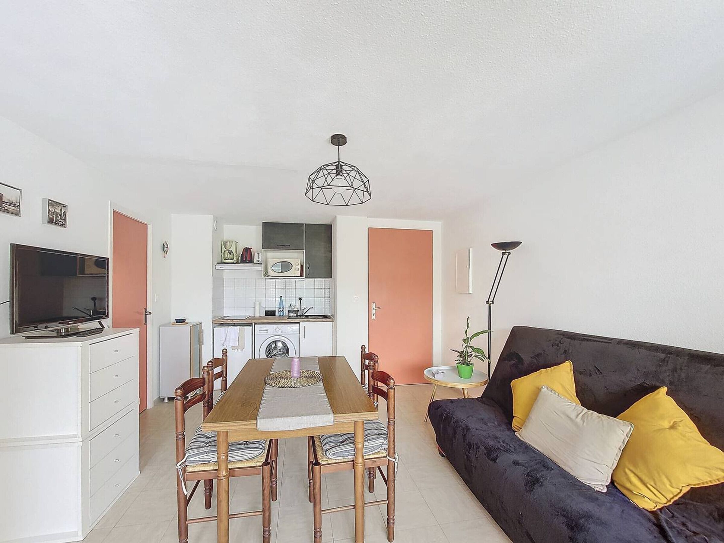 A compact living space with a dining area, kitchenette, and a sofa with cushions.