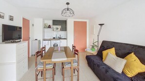 Un espace de vie compact comprenant un coin repas, une kitchenette et un canapé avec des coussins.