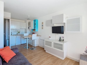 Un espacio habitable compacto con kitchenette, comedor, televisor montado en la pared y un sofá con cojín.