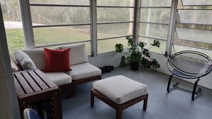 Un solárium con un sofá, un reposapiés, una silla metálica y una planta en maceta.