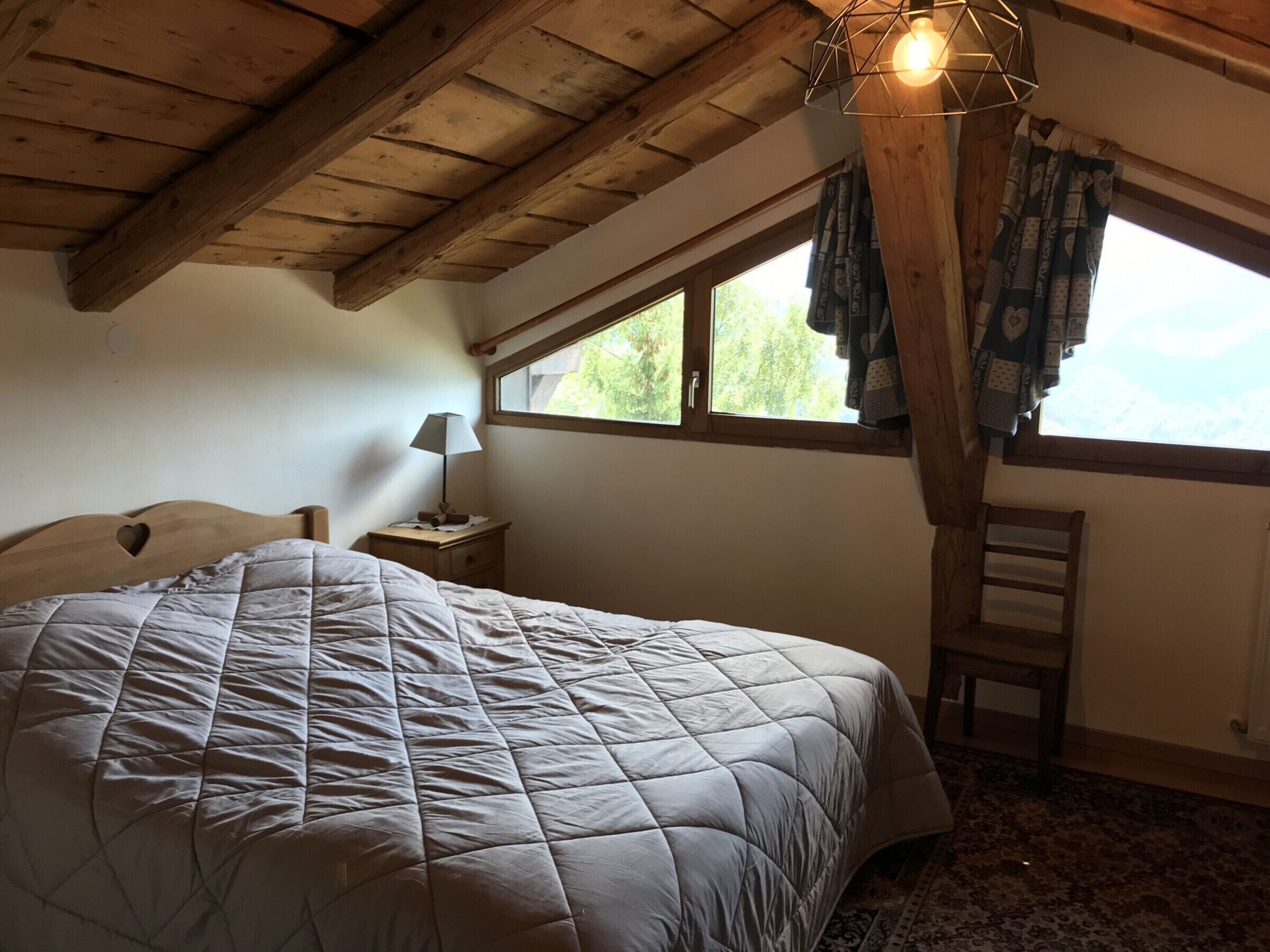 Een slaapkamer met een groot bed, een nachtkastje, een stoel, een raam en een houten plafond.