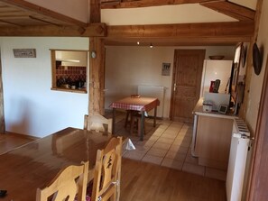 A wooden dining table with chairs, a kitchen area with a refrigerator, and a window with a view of the outside. - Spacious 160m² Apartment - 3 Bedrooms - 10 Guests - Private Parking, WiFi (Arâches-la-Frasse)