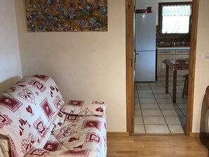 A living room with a sofa, a painting on the wall, and a view into a kitchen with a refrigerator and a window. - Spacious 160m² Apartment - 3 Bedrooms - 10 Guests - Private Parking, WiFi (Arâches-la-Frasse)