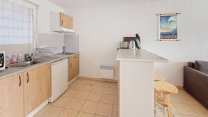 Kompakti keittiö, jossa on keskeinen saareke, sisäänrakennettu uuni ja pieni pesuallas. Seinällä on juliste ja ikkunassa verhot.
