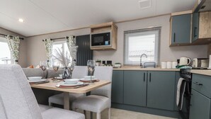 A compact kitchen with a microwave, sink, and oven. There is a dining area with a table set for two and two grey chairs. - The Retreat (Morecambe)