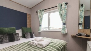 A neatly made bed with striped bedding, a window with curtains, and a mirror on the wall. - The Retreat (Morecambe)